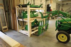 a green tractor parked inside of a garage next to a pile of wood planks