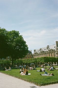 many people are sitting on the grass in front of a large building and some trees