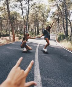 two people riding skateboards down the middle of a road with trees in the background