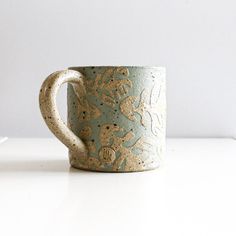 a coffee cup with gold designs on it sitting on a white countertop next to a plant