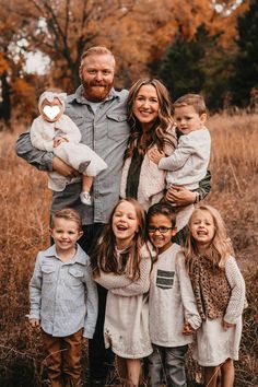 a family posing for a photo in the middle of a field with fall foliage and trees