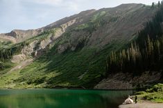 two people sitting on the shore of a mountain lake