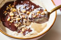 a spoon full of ice cream with nuts and chocolate on top, in a bowl