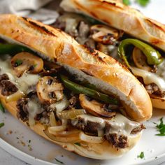 two sub sandwiches are on a plate with cheese and mushrooms in the middle, along with green peppers