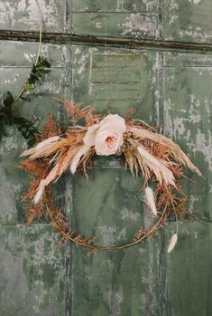 a wreath with dried flowers hanging on a green painted wall next to a planter