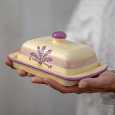 a person holding a casserole dish with purple trim and flowers on the lid