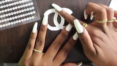 two hands with white manicures and gold rings on top of a wooden table