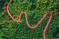 an aerial view of a long red road in the middle of a lush green forest