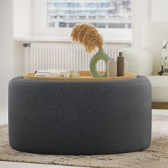 a grey ottoman with a hairbrush and some books on it in front of a window