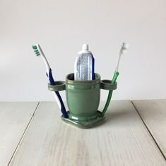 three toothbrushes in a green cup on a white wooden table, with one blue and one green toothbrush holder