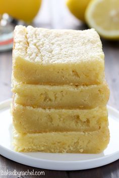 a stack of lemon bars sitting on top of a white plate next to sliced lemons