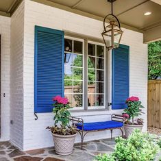 blue shutters on a white brick house with potted plants and bench in front