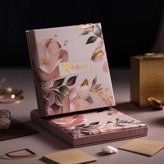 an open box with pink flowers on it next to other boxes and gold foil decorations