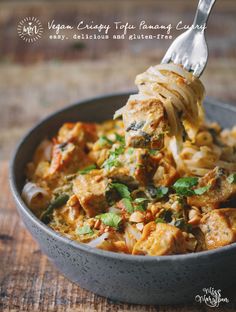 a spoon full of pasta with chicken and spinach in it, on top of a wooden table