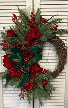 a wreath with red flowers and greenery hanging on a door