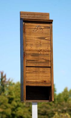 a wooden bird box sitting on top of a white pole in front of some trees