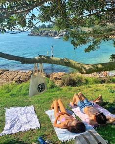 two people laying on towels under a tree near the water