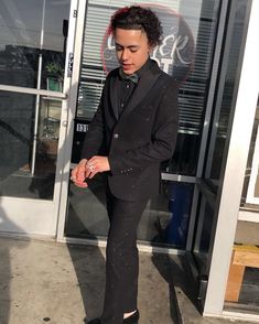 a man in a black suit and tie standing on the sidewalk next to a building