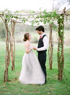 a bride and groom are standing under an arch made out of branches with greenery