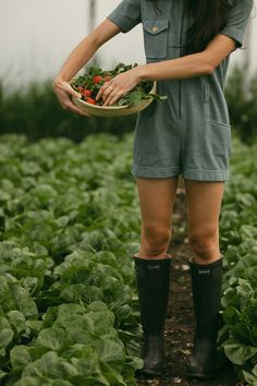 a woman standing in a field holding a bowl of vegetables