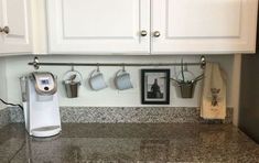 a coffee maker is on the counter next to some cups and mugs hanging from hooks