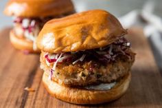 two chicken burgers sitting on top of a wooden cutting board next to each other