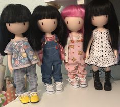 four dolls are standing next to each other on a counter top in front of the wall