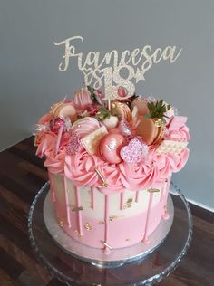 a pink and gold birthday cake decorated with flowers on a clear plate, sitting on top of a wooden table