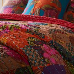 a bed with colorful bedspread and pillows on it's sides, along with an orange comforter