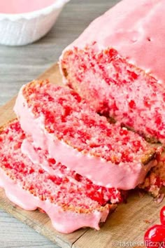 a loaf of cake with pink frosting on a cutting board next to cherries