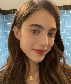 a girl with long brown hair and blue tiles on the wall behind her is smiling at the camera