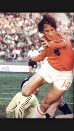 a man kicking a soccer ball on top of a grass field next to a crowd