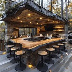 an outdoor bar with stools and lights on the outside wall, in front of trees