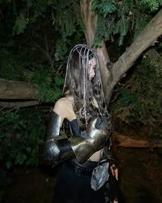 a woman dressed in armor standing next to a tree with chains on her head and hands wrapped around her shoulders