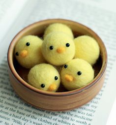 four little yellow chicks in a small bowl on top of an open page of a book