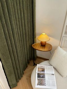 a small table with a lamp on top of it next to a window covered in green curtains