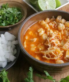 some food is in bowls on a wooden table with limes and cilantro