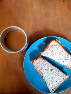 two pieces of bread sit on a blue plate next to a cup of coffee