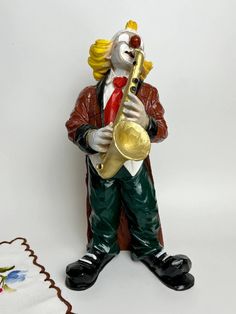 a ceramic figurine of a clown holding a trumpet and wearing a red hat