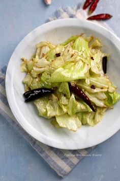 a white bowl filled with lettuce on top of a blue table cloth next to red chili peppers