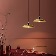 three lights hanging over a dining table with flowers and glasses on the table next to it