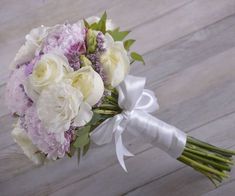 a bouquet of white and purple flowers on a wooden floor with a ribbon tied around it