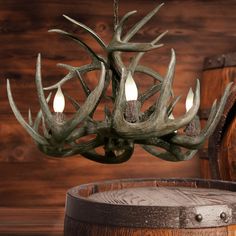 an antler chandelier hanging from a wooden barrel with three candles in it