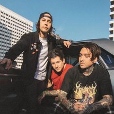 three young men are posing in front of a car