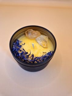 a black bowl filled with yellow liquid and blue flowers on top of a white table