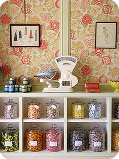 an assortment of candy sits on a shelf in front of a wallpapered wall