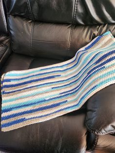 a crocheted blanket sitting on top of a black leather chair next to a pillow