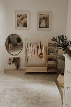 a white room with two pictures on the wall and clothes hanging in front of a mirror