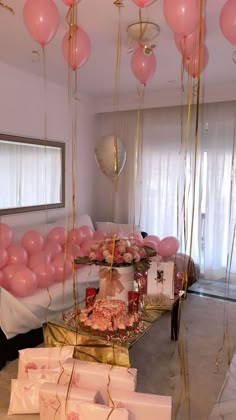 pink and gold balloons are hanging from the ceiling above a table filled with gift boxes