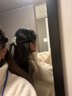 two women standing in front of a mirror with their hair styled into a pony tail